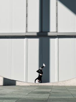 A person performs a handstand against a modern urban building wall, showcasing balance and acrobatics.