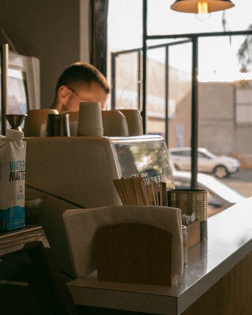 Free A cozy urban café scene showing a barista working behind the counter with sunlight streaming through the windows. Stock Photo