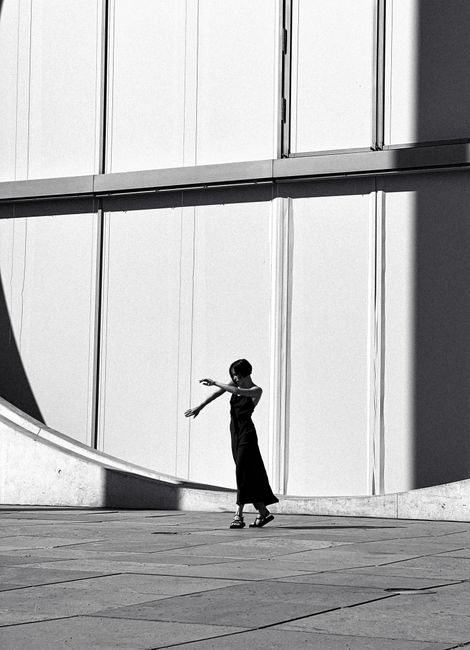 Black and white photo of a woman walking in front of a modern building facade.