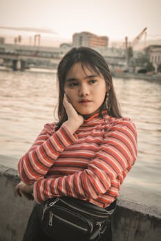 一名年轻女子穿着条纹毛衣，在城市河畔若有所思地摆姿势