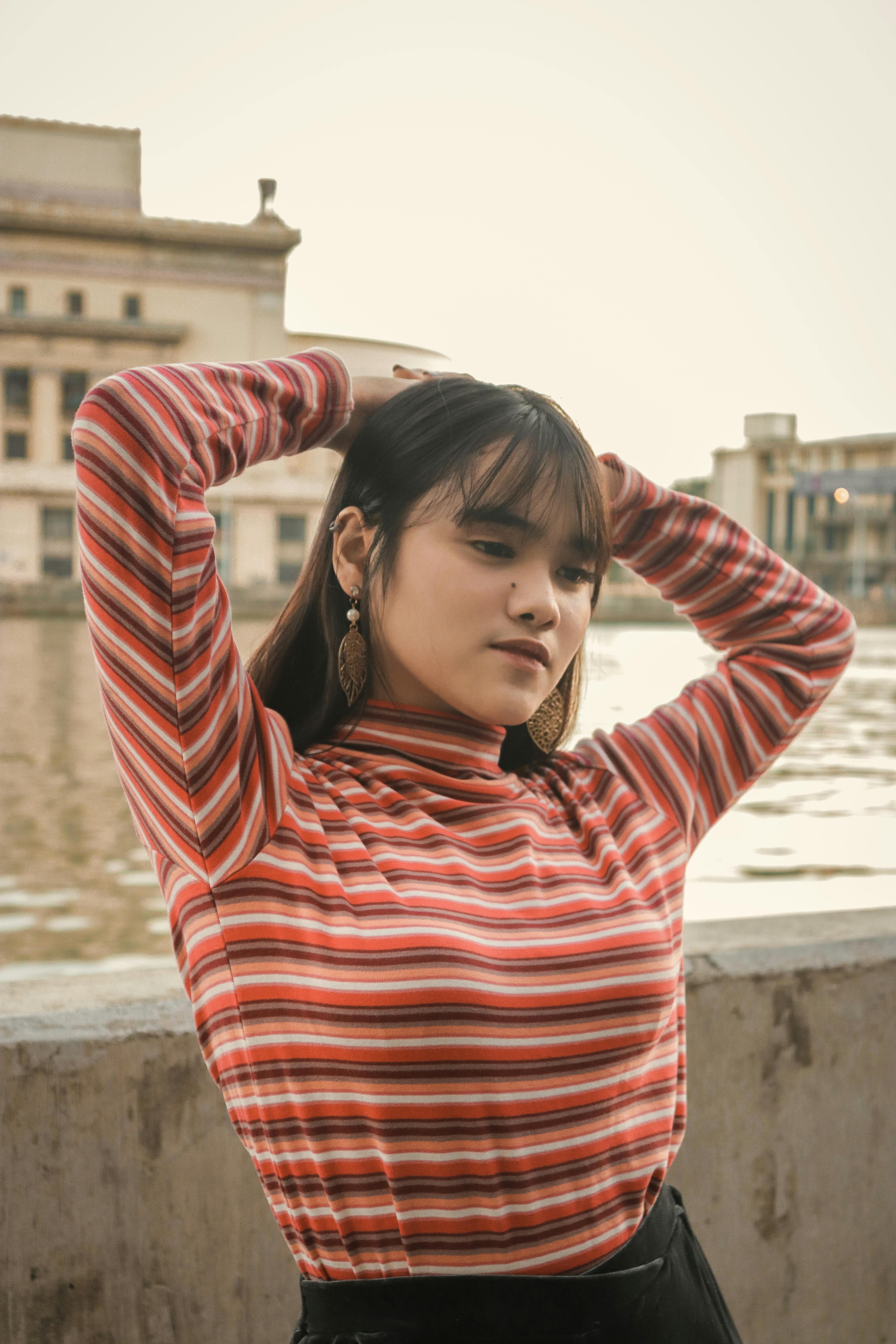 一位身穿条纹上衣的年轻女子在城市河畔摆出姿势，这是一幅时尚的日光肖像