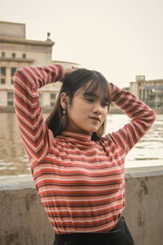 一位身穿条纹上衣的年轻女子在城市河畔摆出姿势，这是一幅时尚的日光肖像