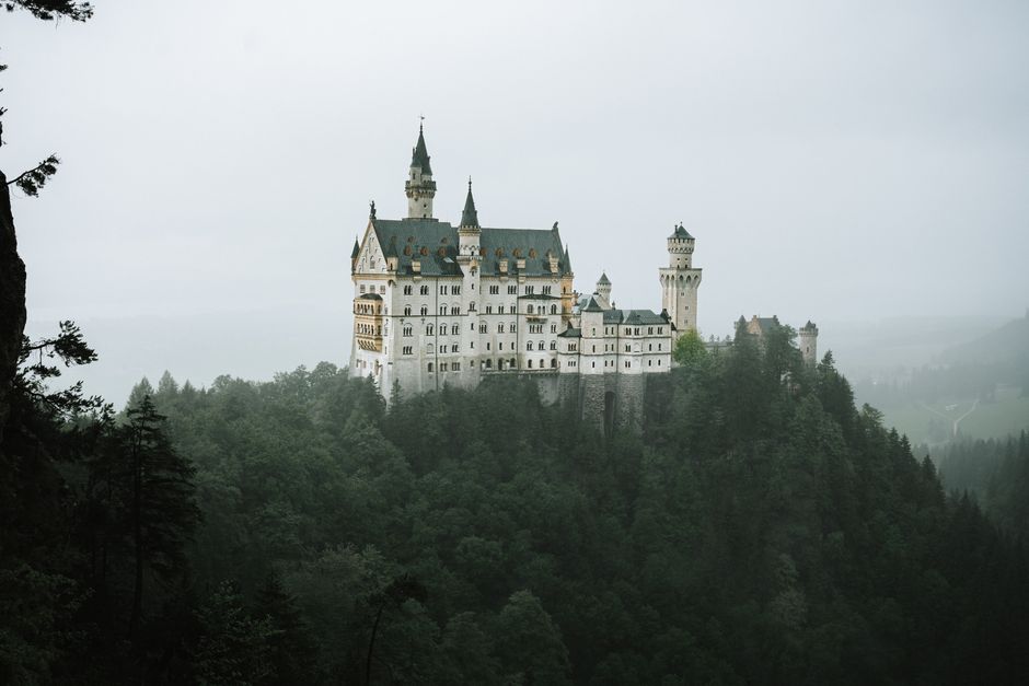 Aerial view of Neuschwanstein Castle amid a foggy forest in Bavaria, Germany.
