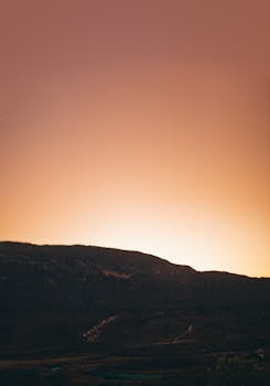 A beautiful sunset casting a warm glow over a mountainous silhouette, perfect for nature lovers.