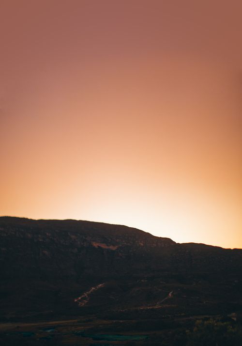 Free A beautiful sunset casting a warm glow over a mountainous silhouette, perfect for nature lovers. Stock Photo