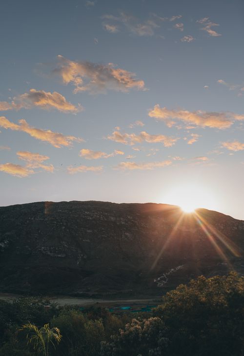 Free Stunning sunset view with sun rays over a serene mountain landscape and scattered clouds. Stock Photo