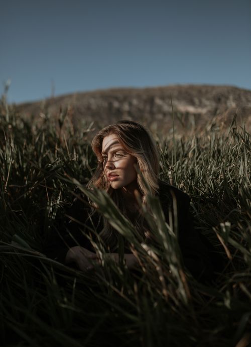 Free Portrait of a young woman sitting in a meadow, bathed in soft sunlight, capturing a serene outdoor moment. Stock Photo