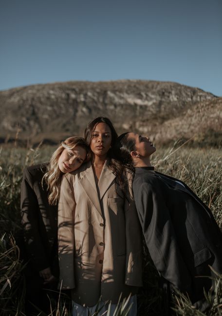 Three women posing in stylish suits in a field, capturing a fashionable and elegant look.