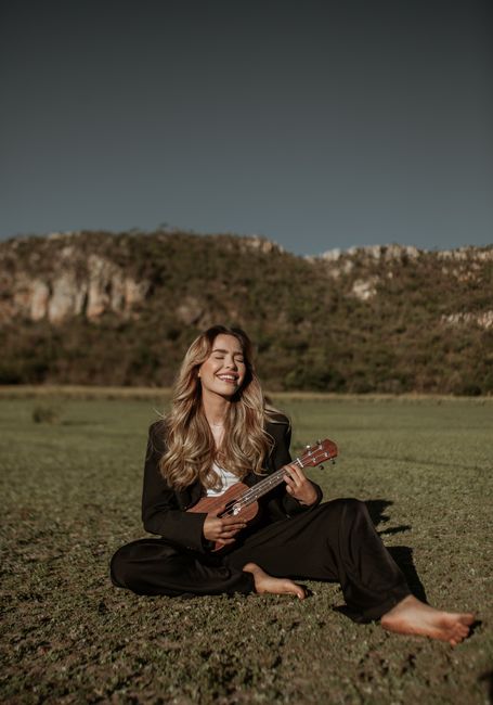 Woman in a black suit playing guitar in a meadow, smiling blissfully.