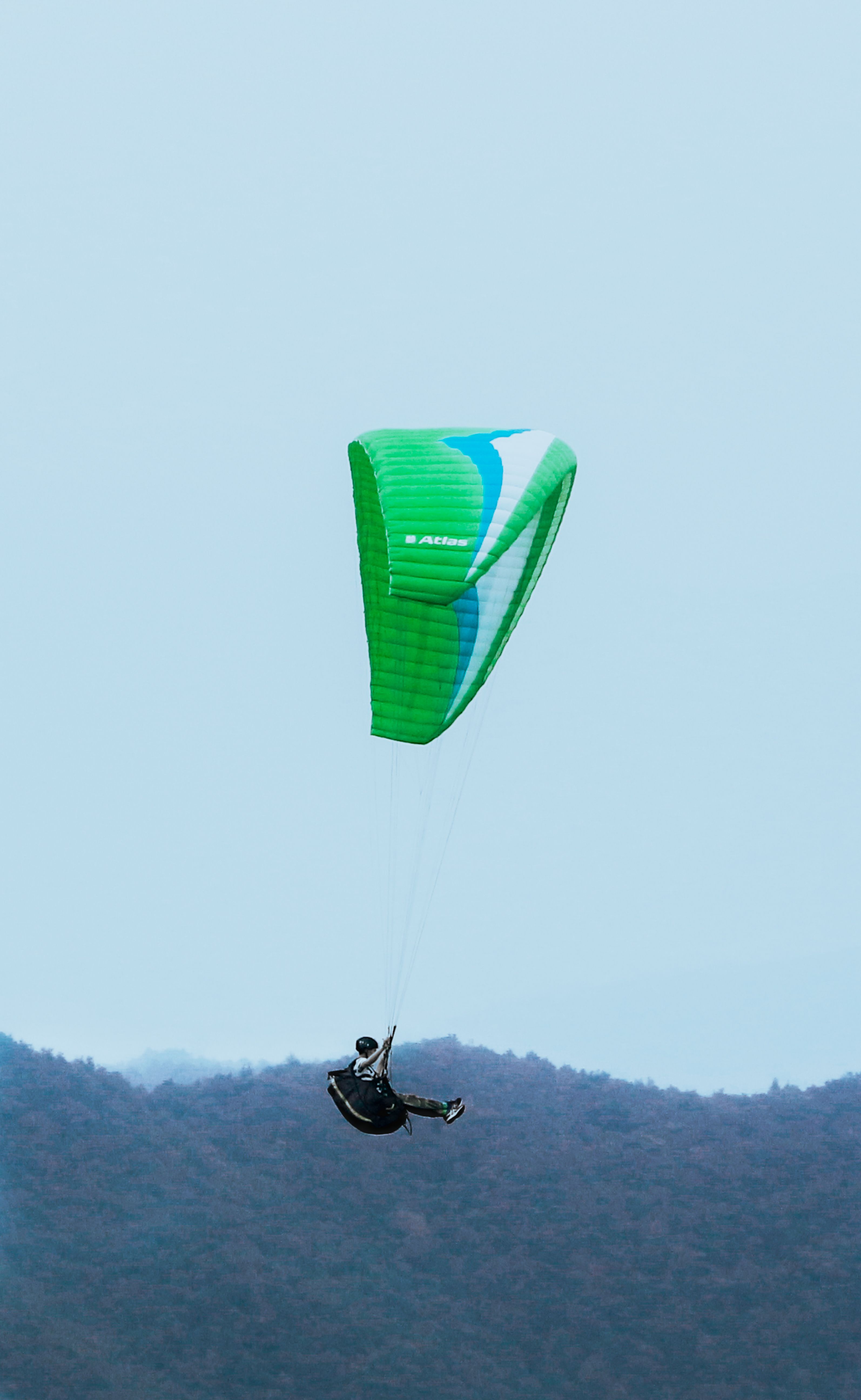 Experience the thrill of paragliding above scenic hills with this vibrant green parachute.