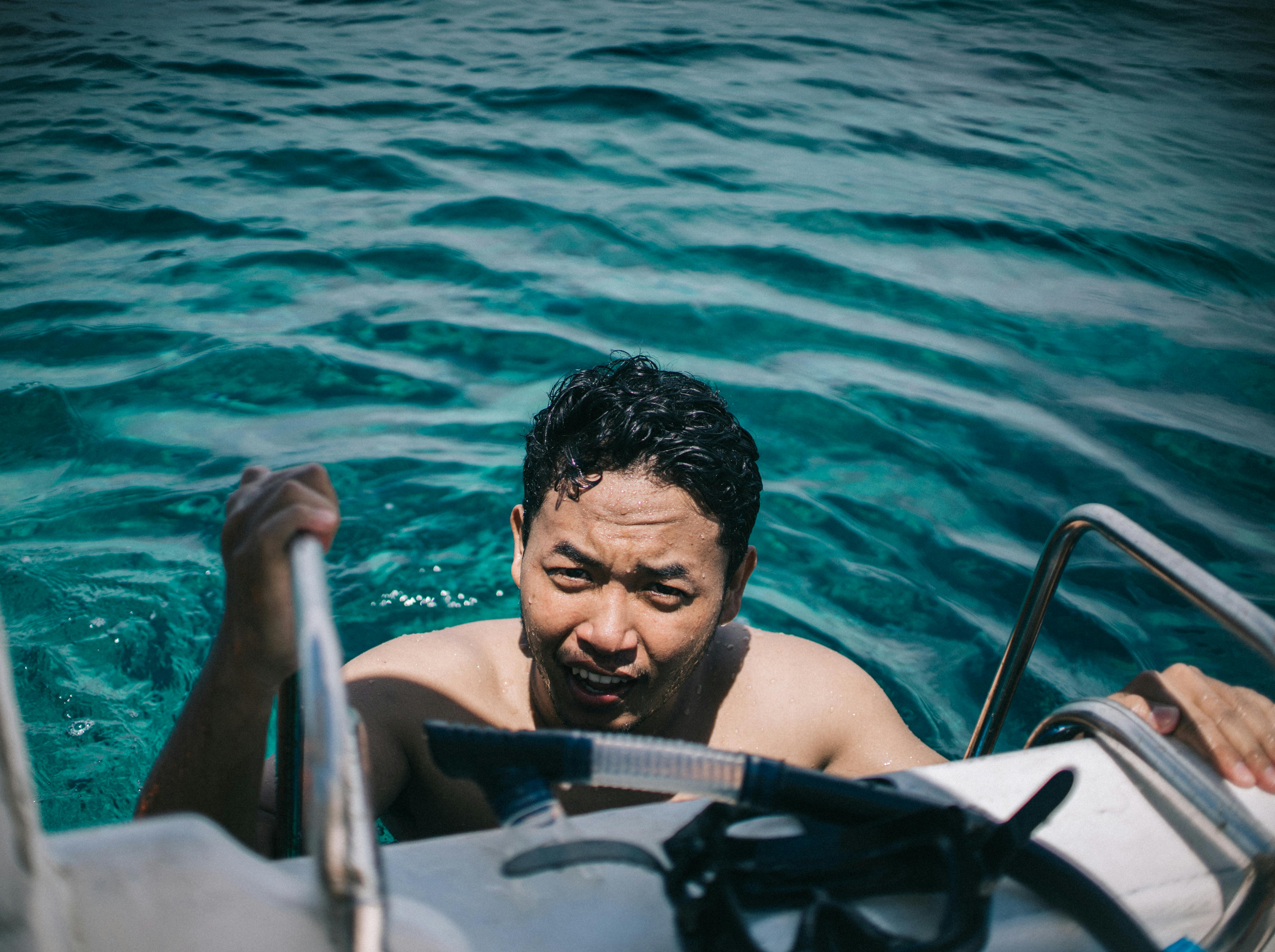 晴朗的热带水域中，成年雄性游泳后爬上了梯子，天空晴朗