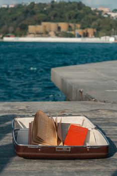 Open suitcase with books on pavement by the sea in İstanbul, Türkiye.
