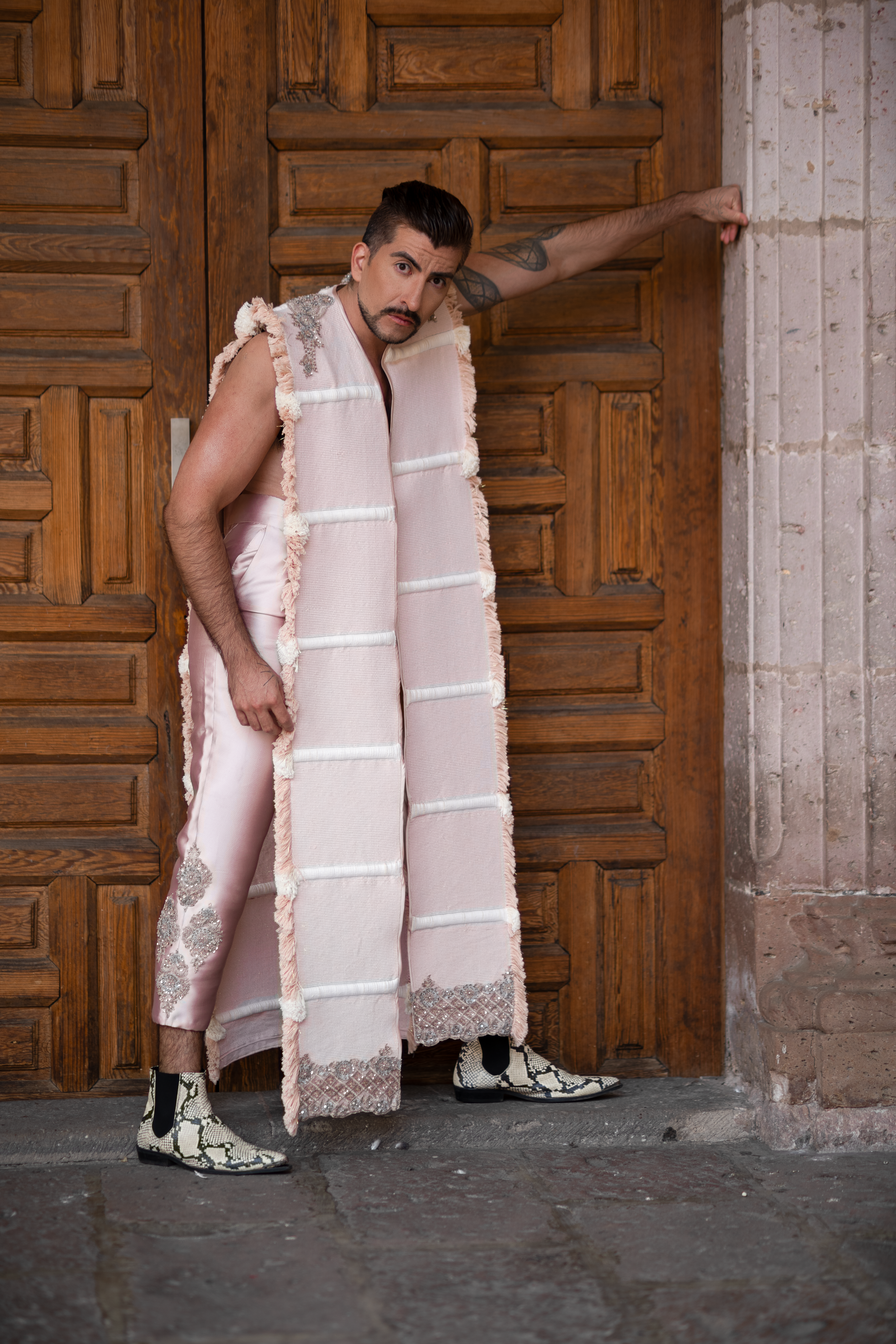 A man in traditional attire poses confidently by a carved wooden door, exuding cultural charm.