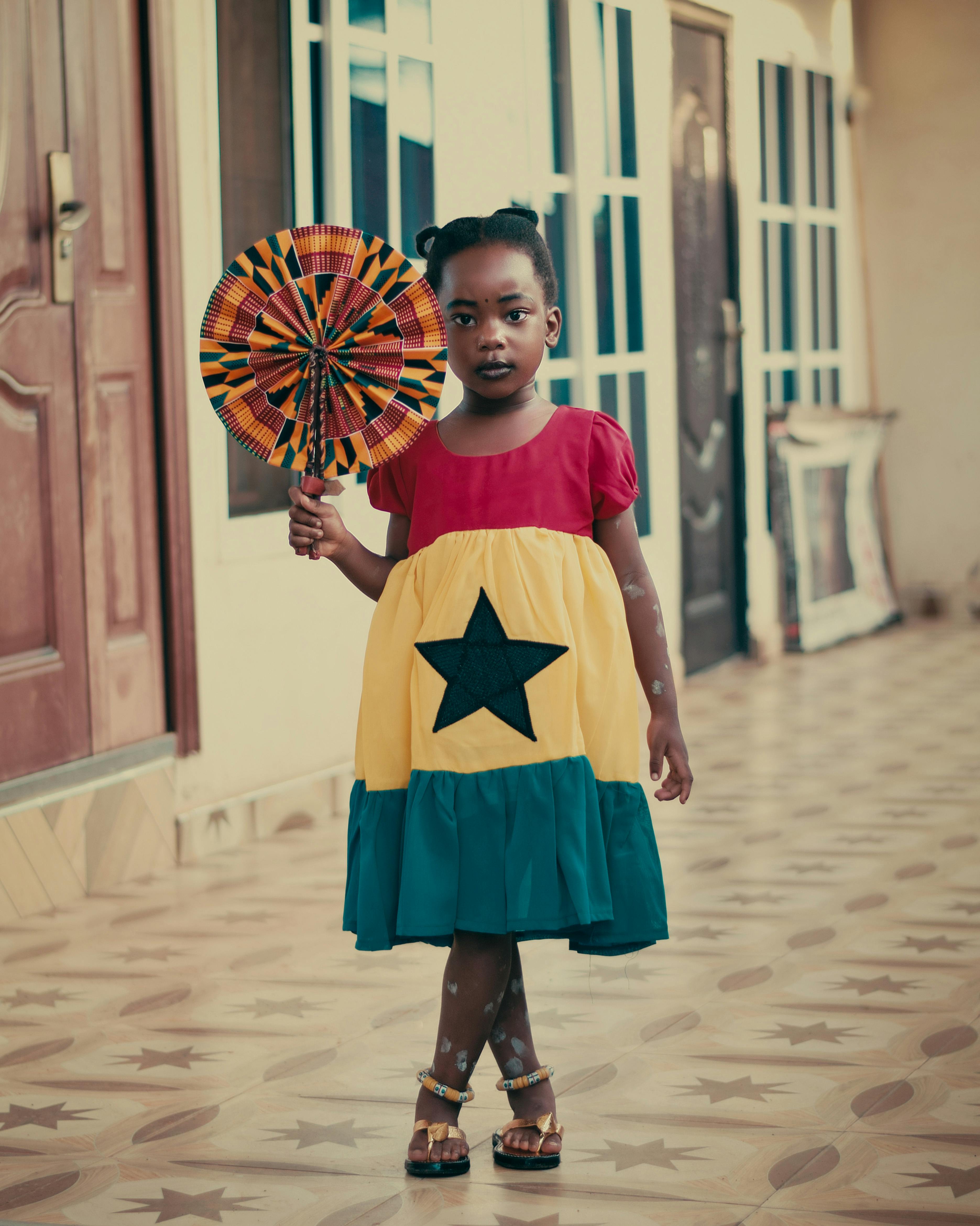 A little girl in a dress holding a fan Free Stock Photo