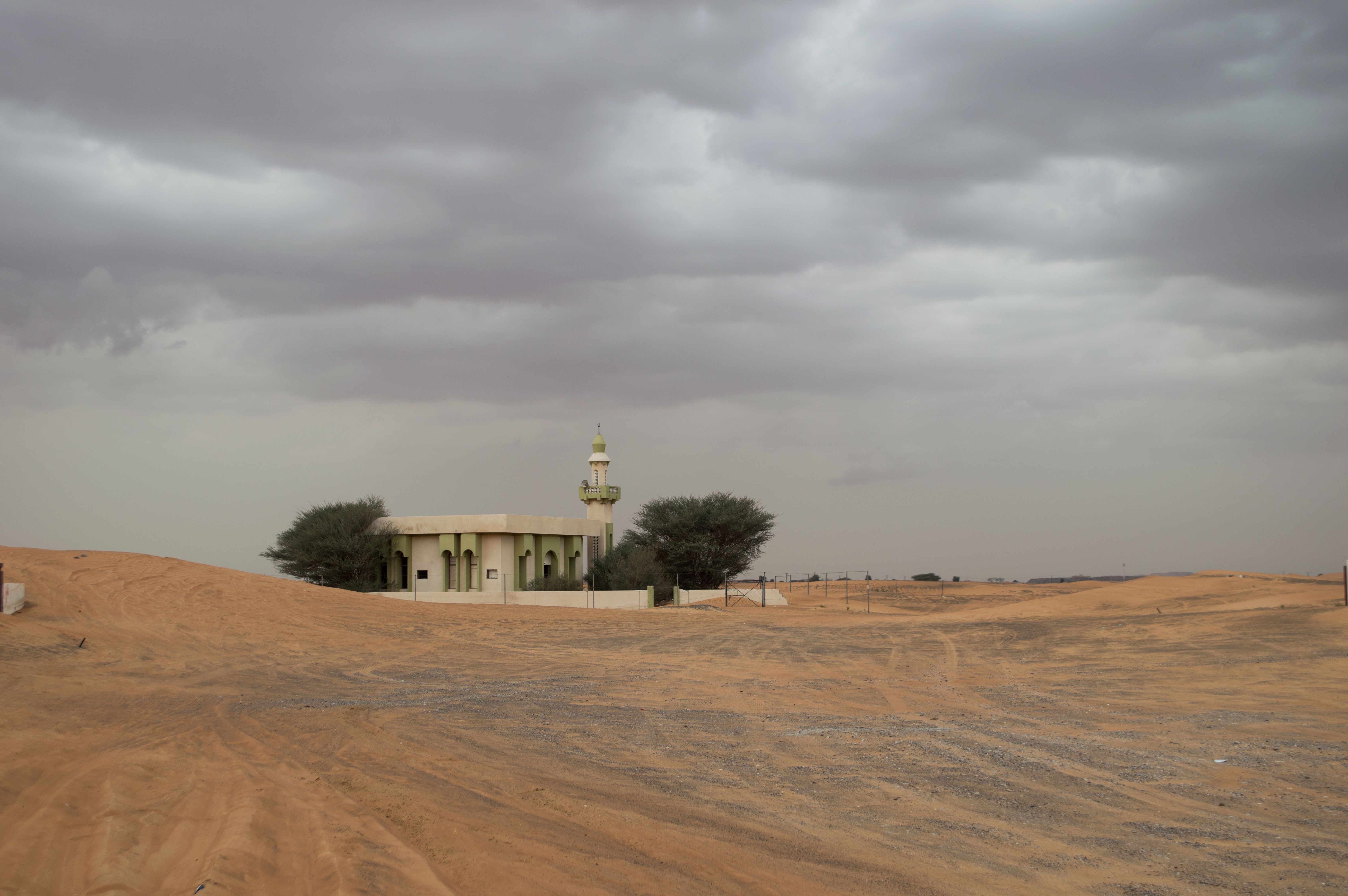 A solitary mosque stands in the desert of Al Madam, UAE under a cloudy sky.