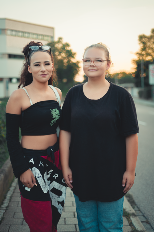 Free Two friends standing on a city sidewalk during sunset, smiling. Stock Photo