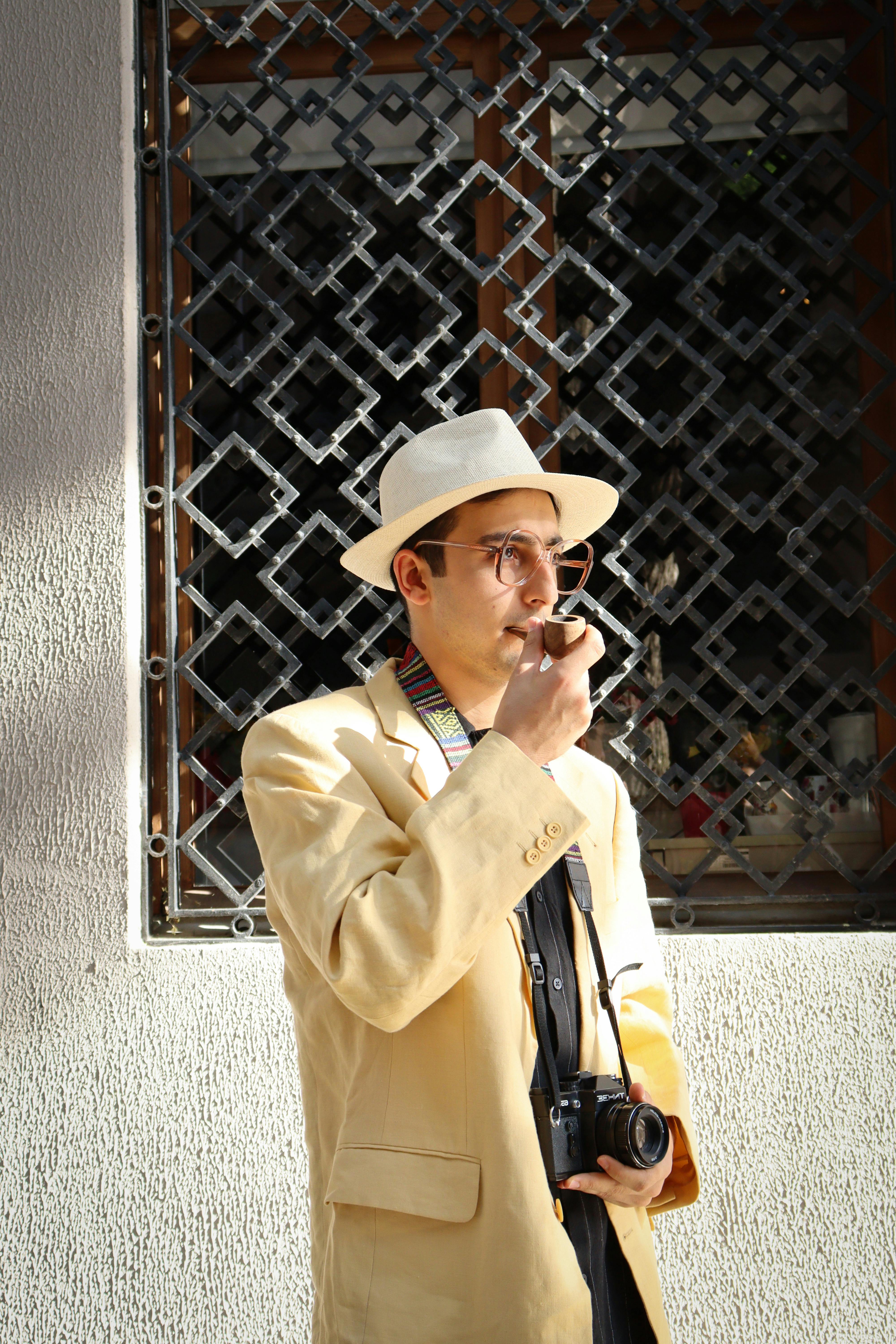 Fashion-forward man with hat and camera, captured outdoors in an urban setting.