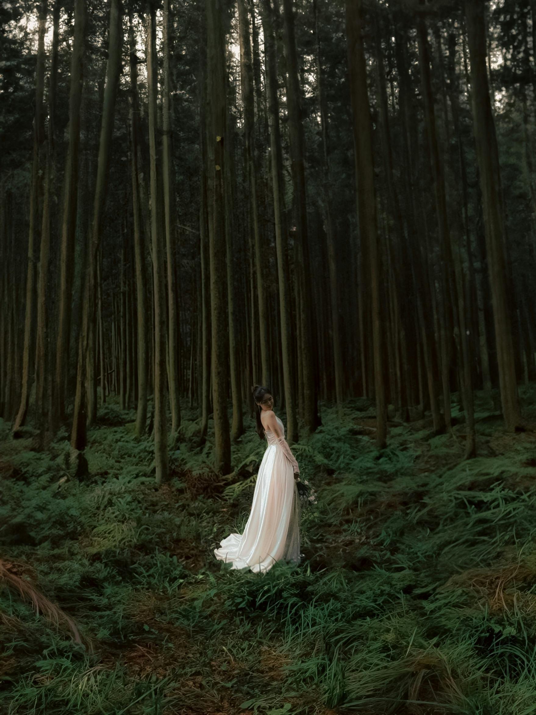 A bride stands gracefully in a lush, dense forest, capturing a serene moment in nature.