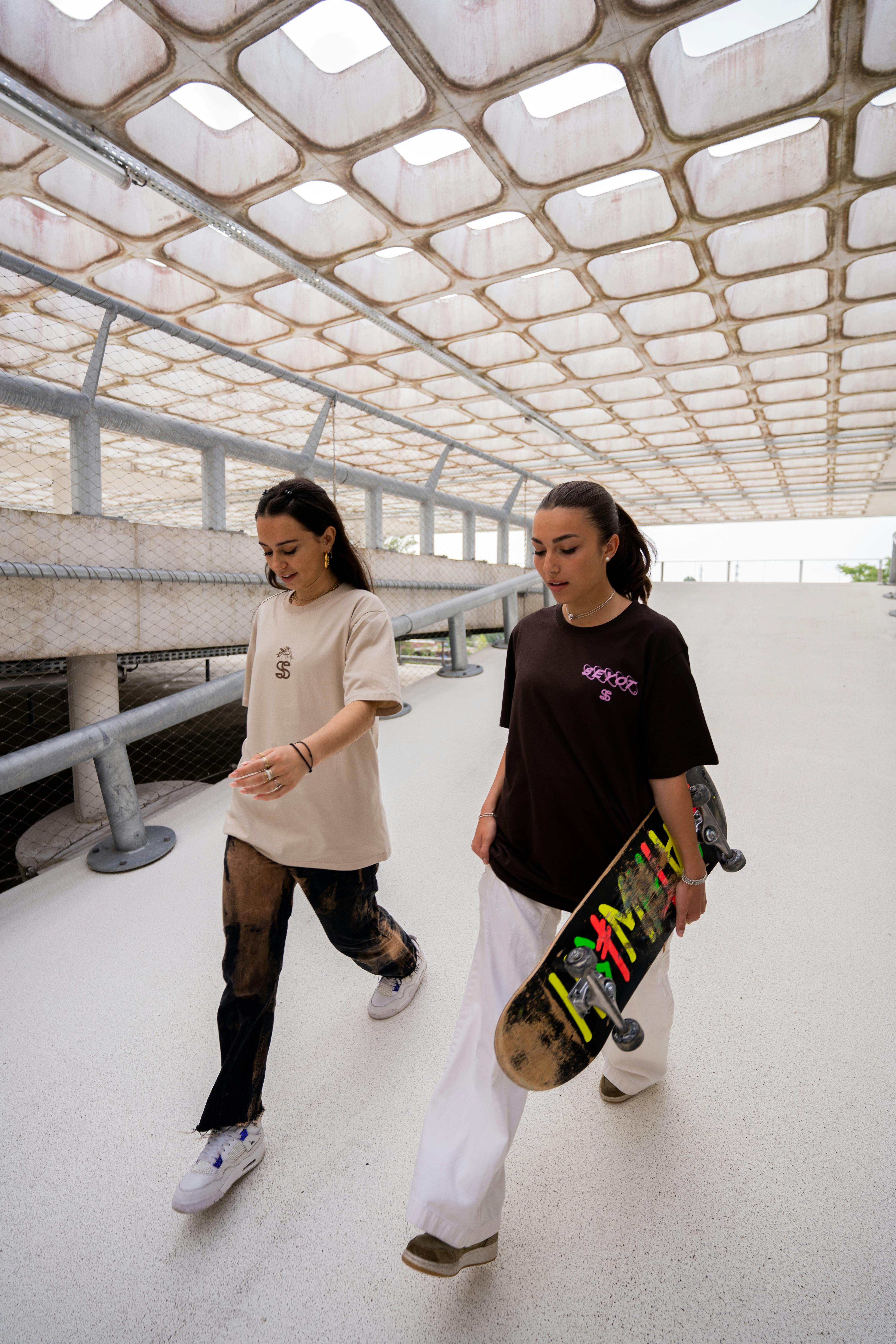 Two women walking with skateboards in an urban setting in Bordeaux, France.