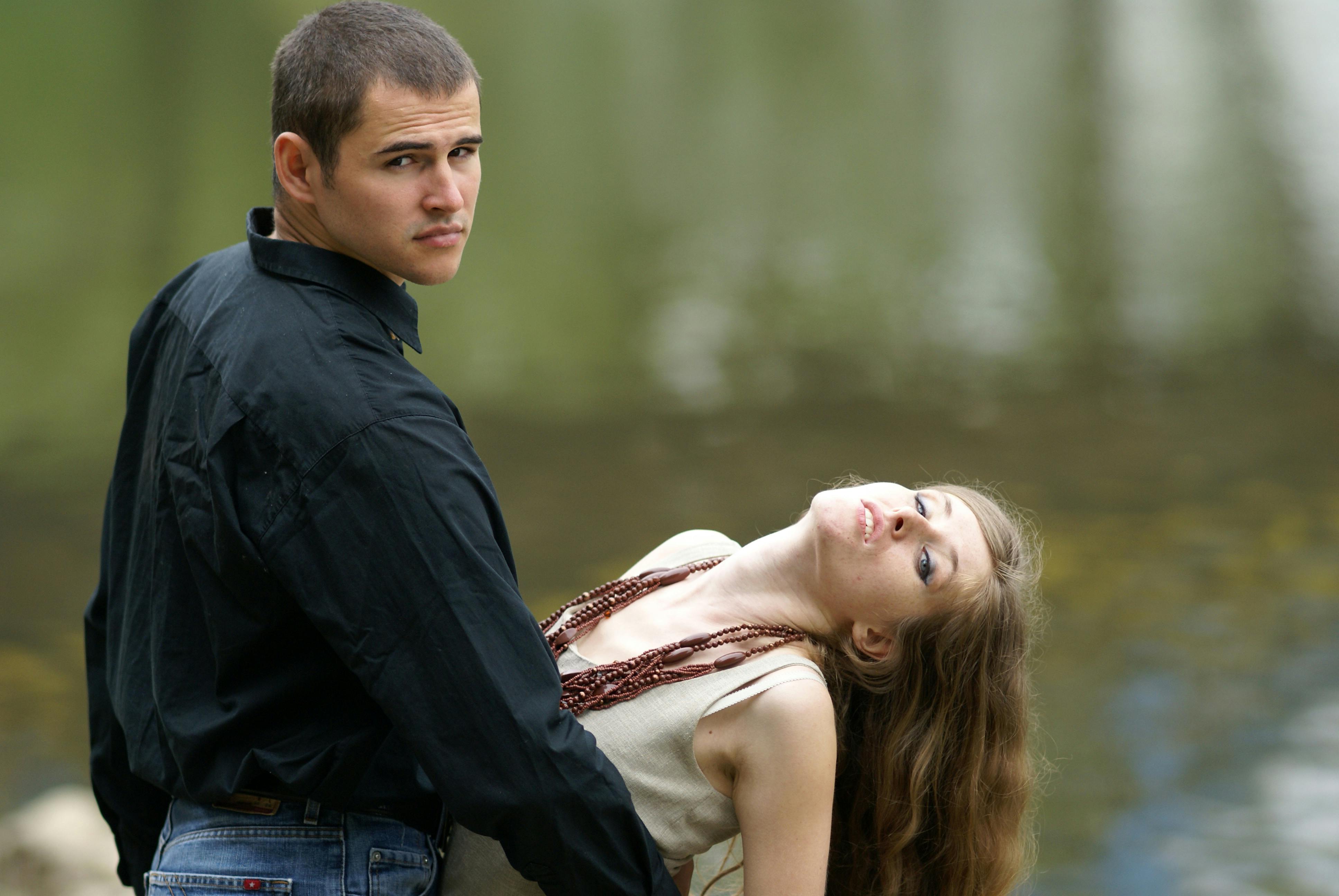 A young couple posing by a serene lake, showcasing fashion and elegance outdoors.