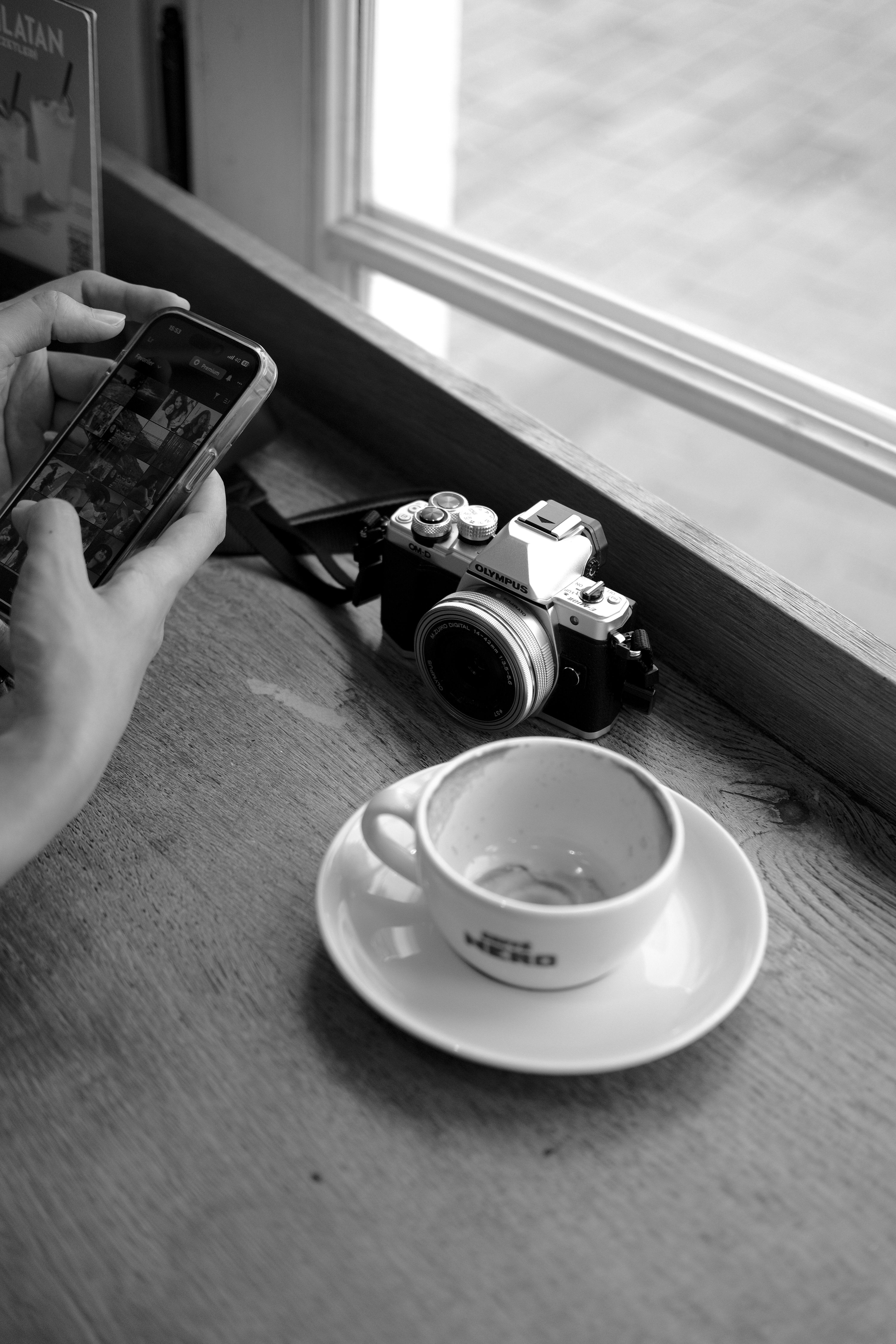 Black and white photo of a café table with a coffee cup, camera, and smartphone.