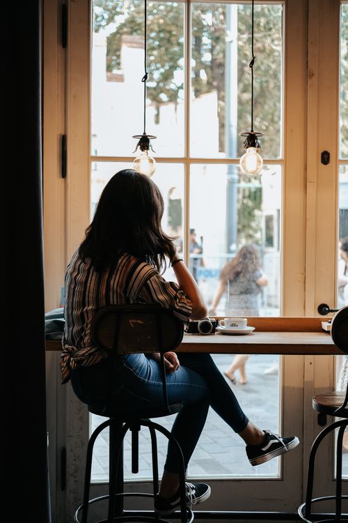 Free A woman sits in a cozy cafe by the window, looking outside. Soft lighting adds to the serene atmosphere. Stock Photo
