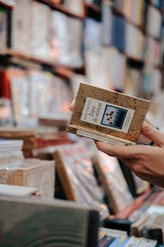 Close-up of a hand holding a book in a cozy, warm bookstore with shelves of books in the background.