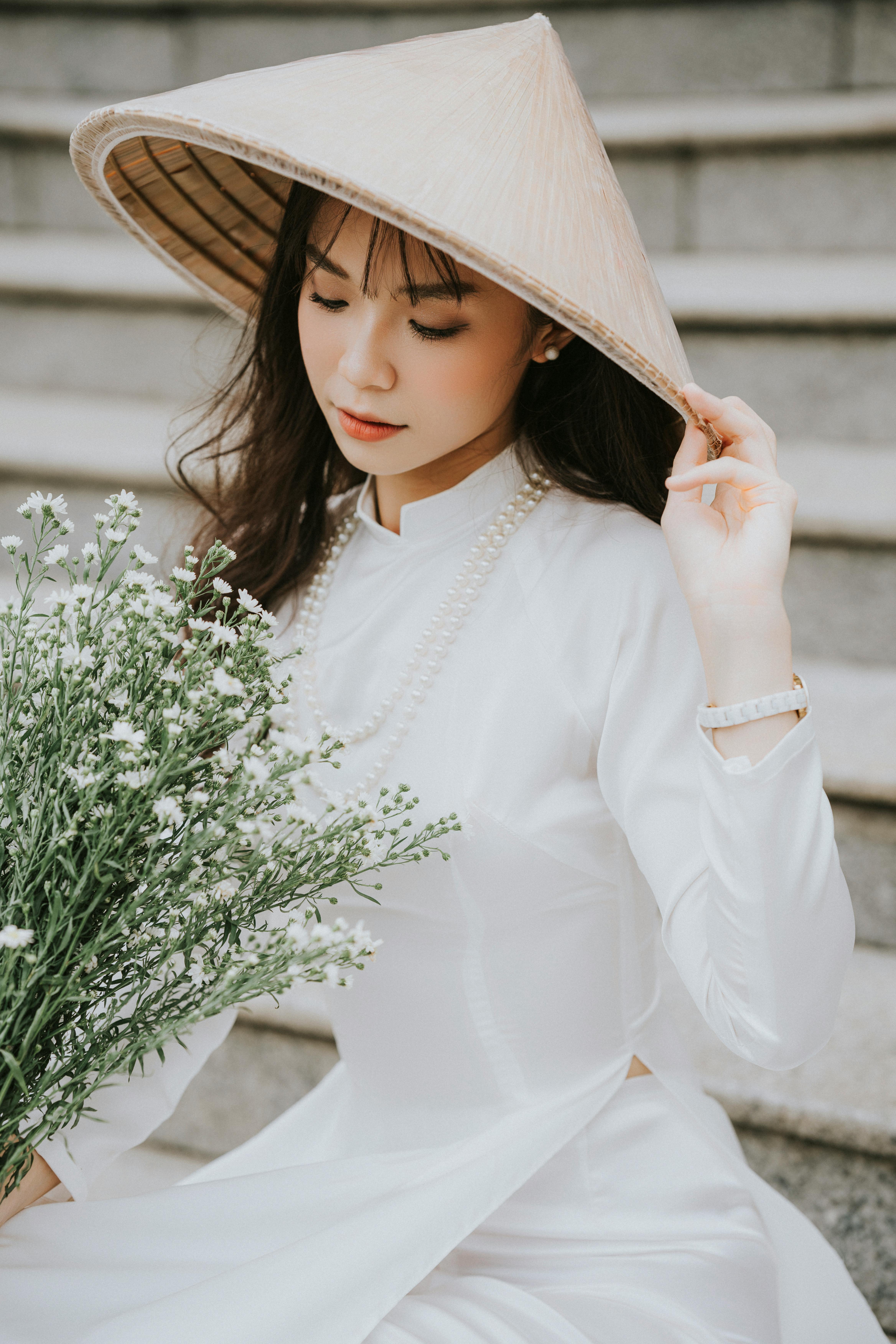 Graceful portrait of an Asian woman in traditional clothing with a conical hat and bouquet.