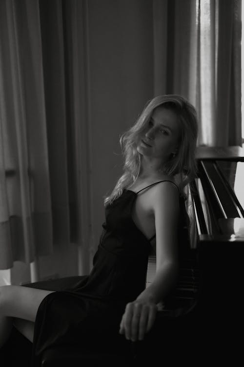 Black and White Photo of a Blond Woman Leaning on a Piano