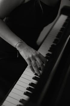 A woman's hand elegantly plays piano keys in a monochrome artistic shot.