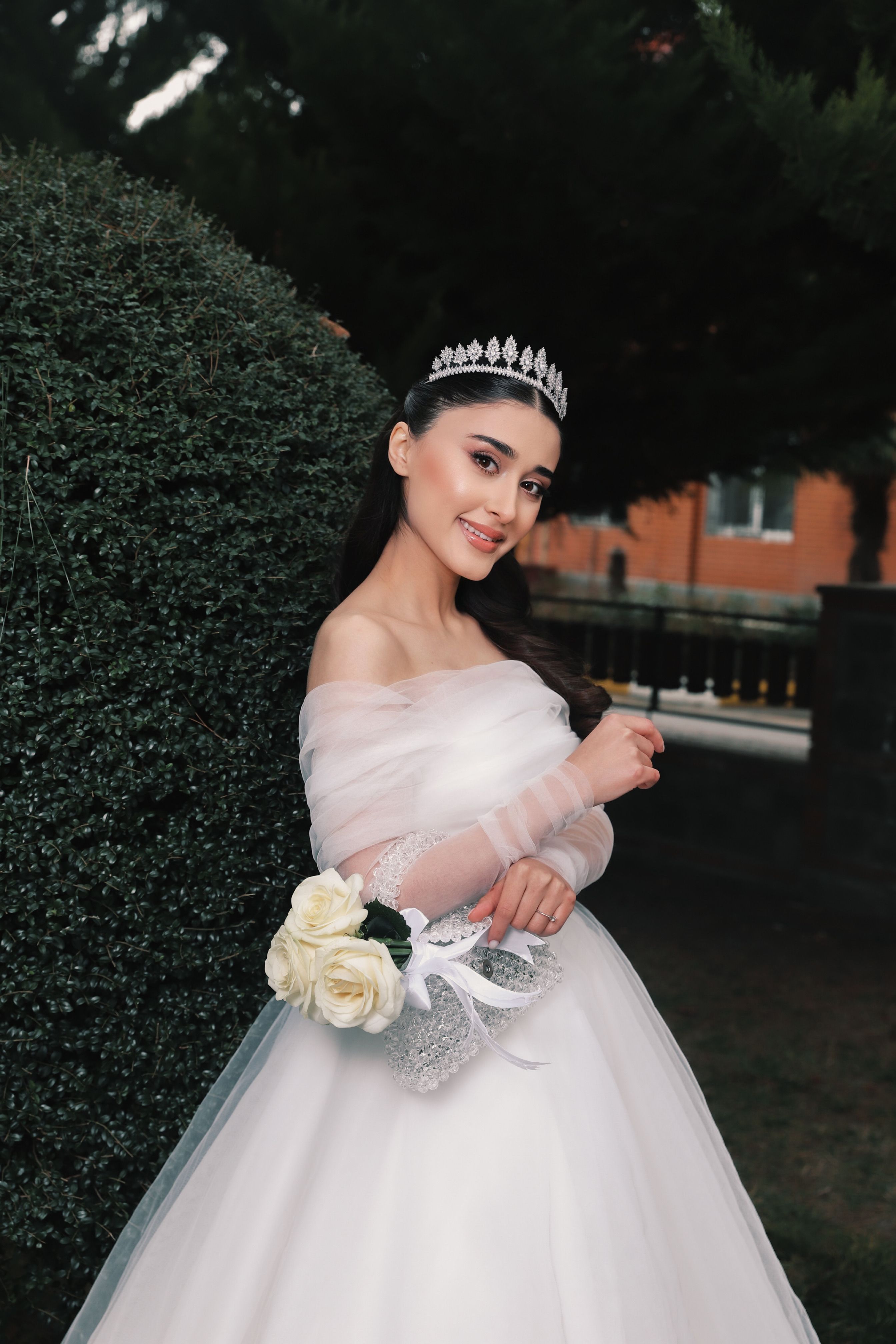A beautiful bride in a stunning wedding gown smiling and holding a floral bouquet outdoors.