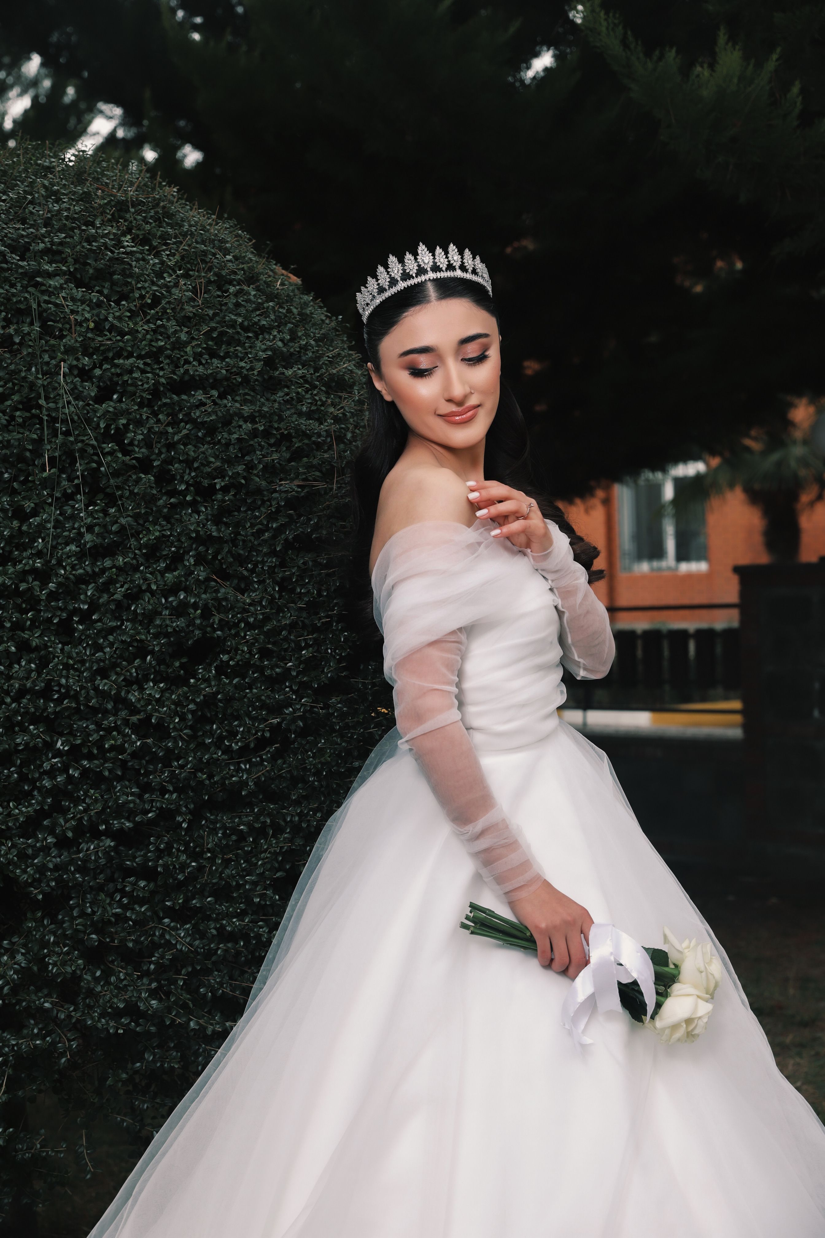Graceful bride in wedding dress holding a flower bouquet outdoors.