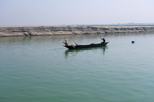 Free Two men fishing on a boat in a serene river setting during the day. Stock Photo