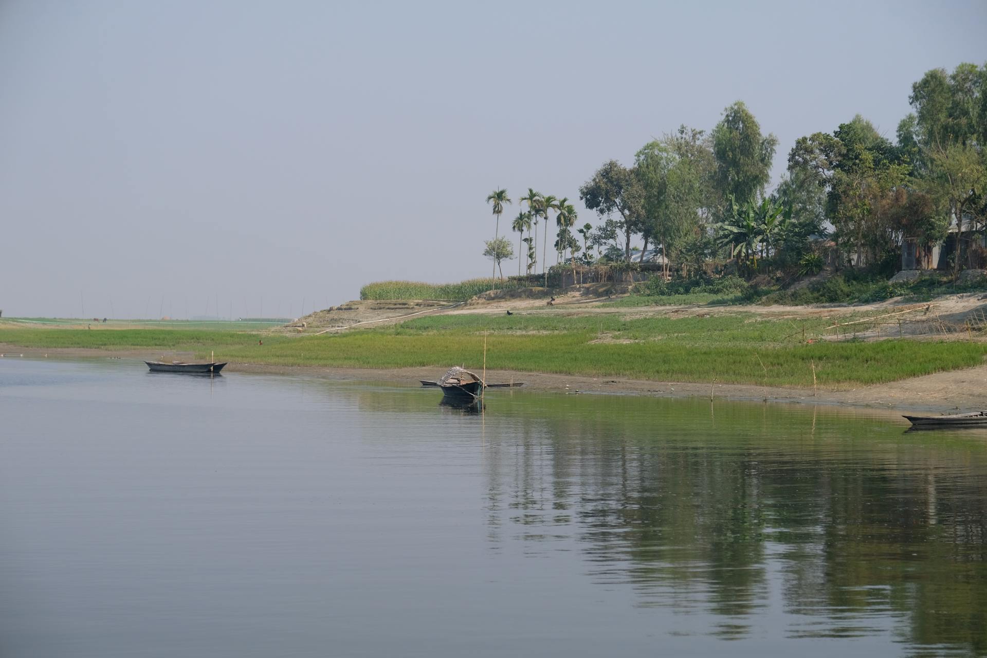 A serene riverside scene featuring boats and lush green surroundings in a rural setting.