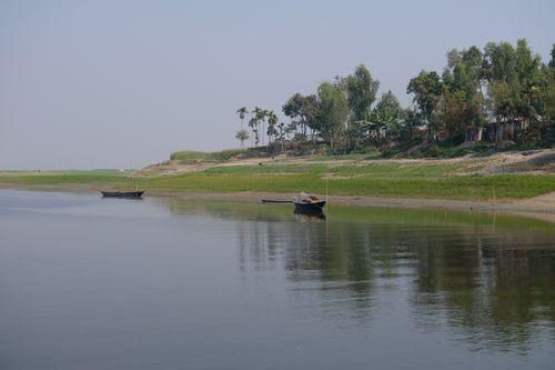Free Peaceful rural riverside scene with small boats and lush green trees under a clear sky. Stock Photo