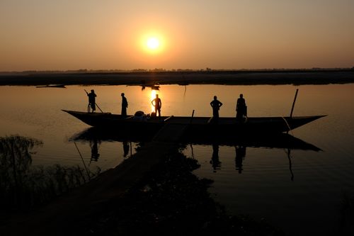 Free A serene sunset silhouette of a boat and people on a tranquil lake. Stock Photo