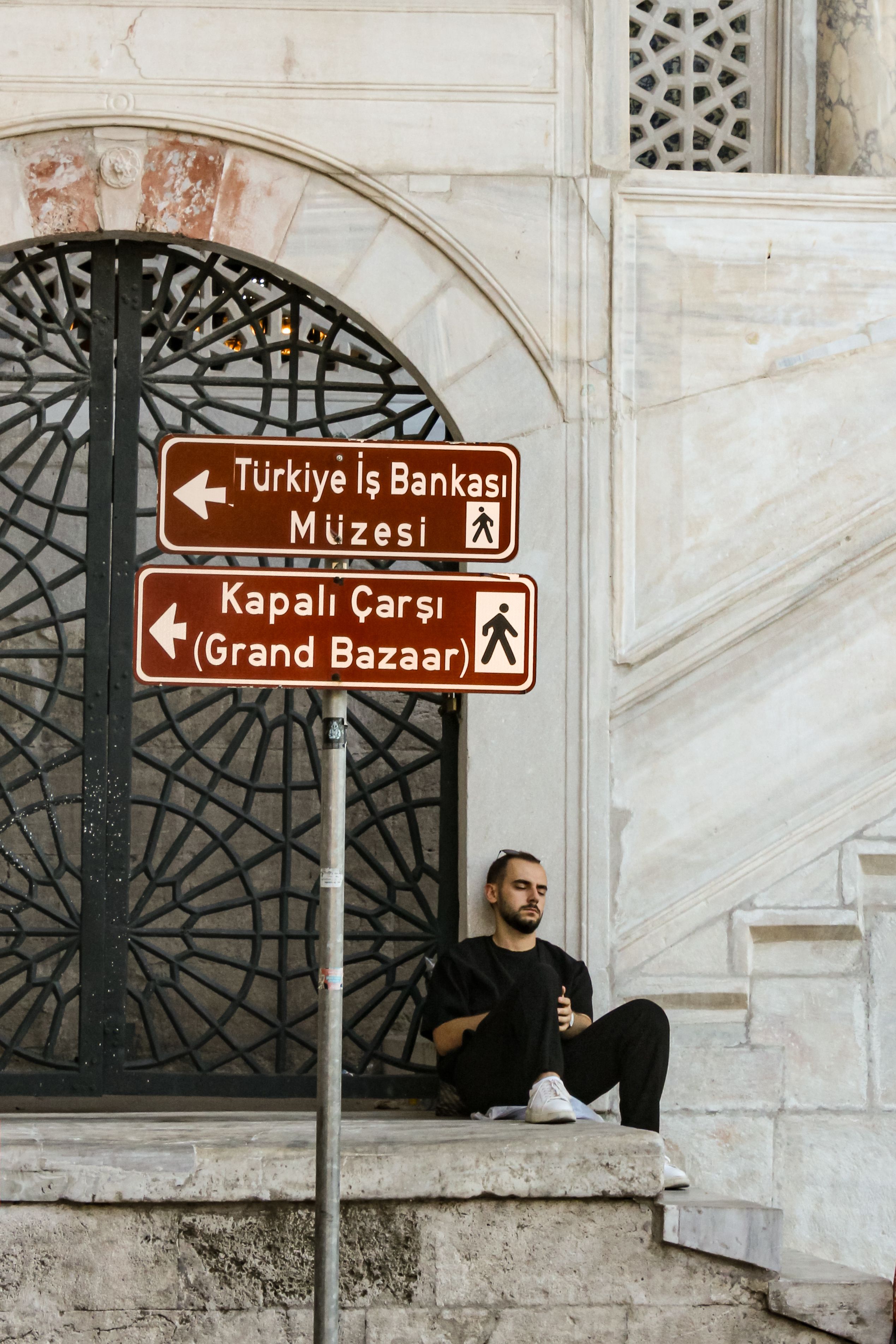 Man Sitting near Directional Signs in Istanbul · Free Stock Photo