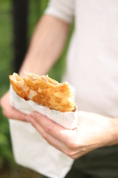 Close-up of a man holding a crispy pastry outdoors in daylight.