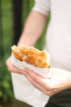 A person enjoys a crispy pastry in bright sunlight, showcasing outdoor dining.