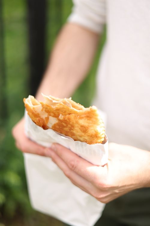 Free A person enjoys a crispy pastry in bright sunlight, showcasing outdoor dining. Stock Photo