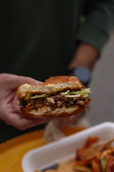 Mouthwatering beef burger with toppings held by a person outdoors, perfect for lunch.