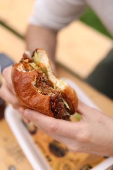 Appetizing beef burger with fresh ingredients being held by a diner outdoors.