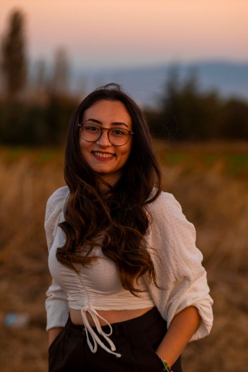 Free A woman with glasses and long hair smiling outdoors at sunset. Stock Photo