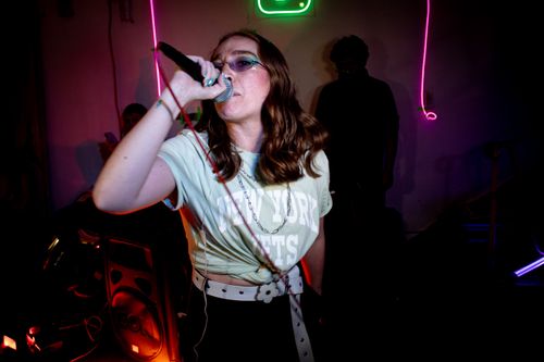 Free Energetic female singer performing live in a neon-lit nightclub setting, showcasing vibrant nightlife vibes. Stock Photo