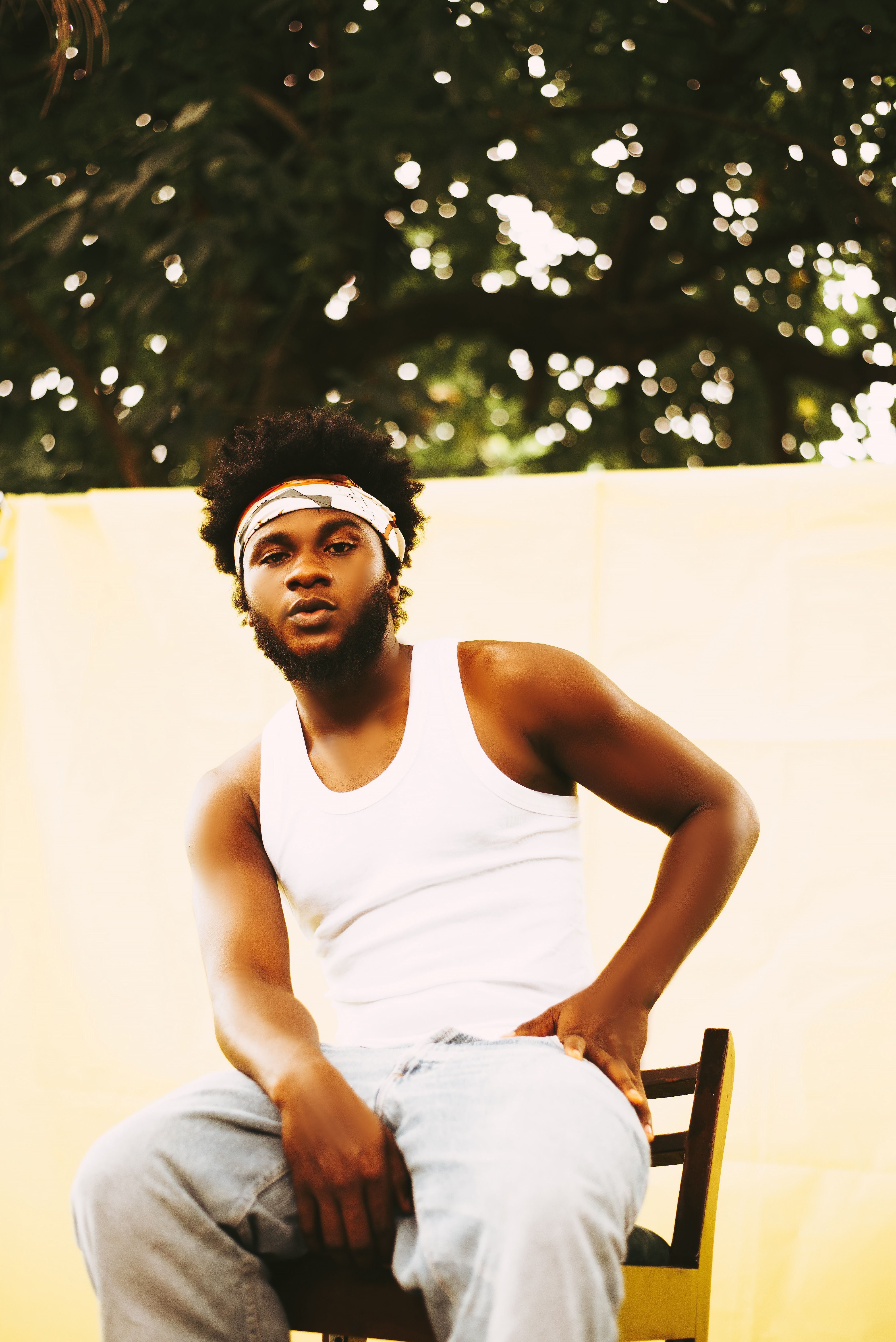 Young man with curly hair sitting outdoors wearing a tank top, exuding a relaxed and contemplative mood.