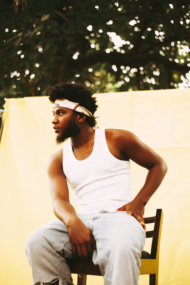 A Young Man In A Tank Top Sitting Outside 