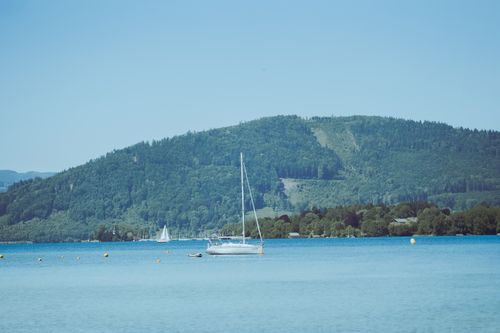 Free A tranquil scene of sailboats on a serene lake against a backdrop of lush, green hills under a clear blue sky. Stock Photo