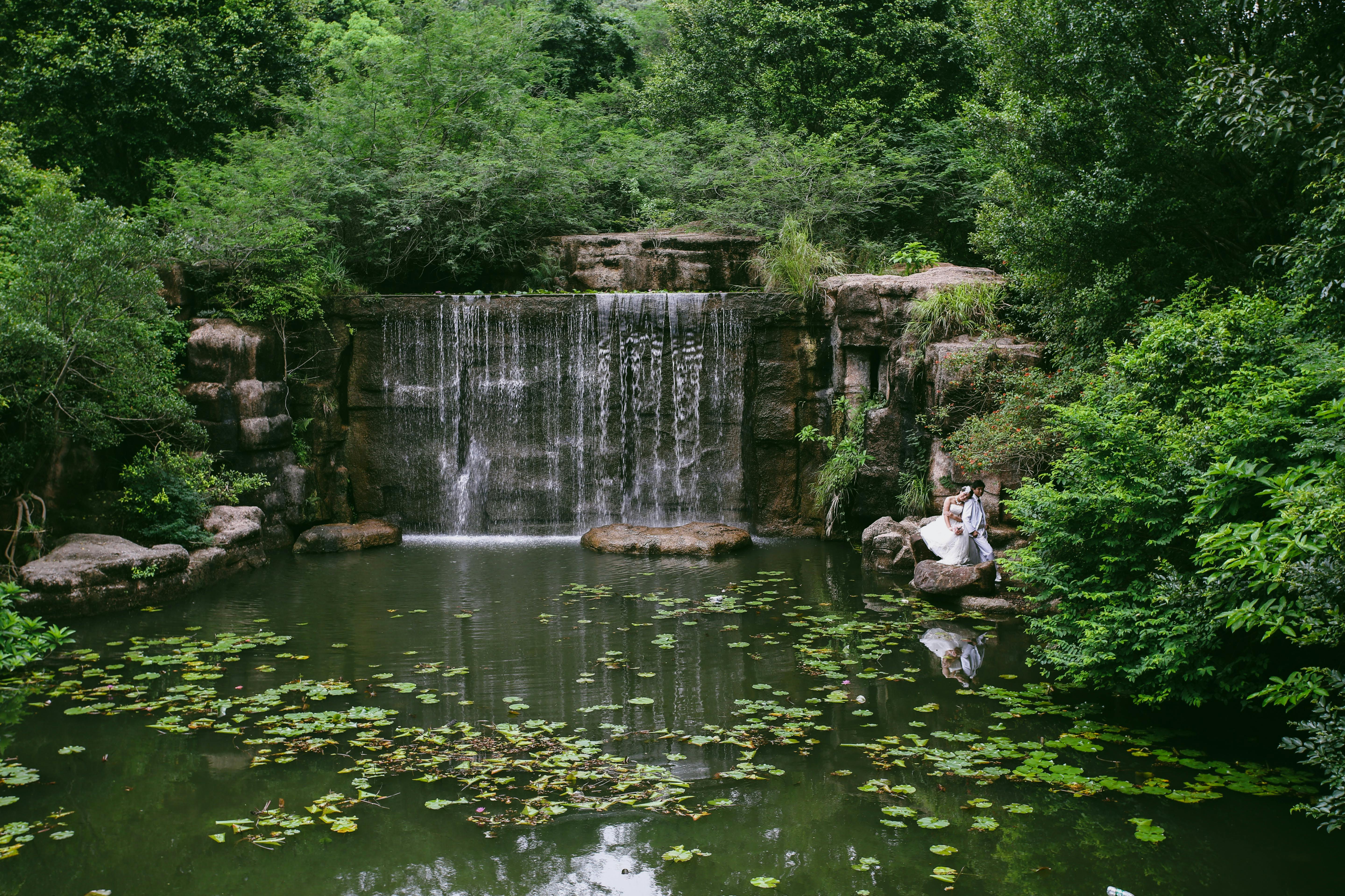 Jeunes mariés assis près d’une cascade paisible en forêt, ambiance calme et claire