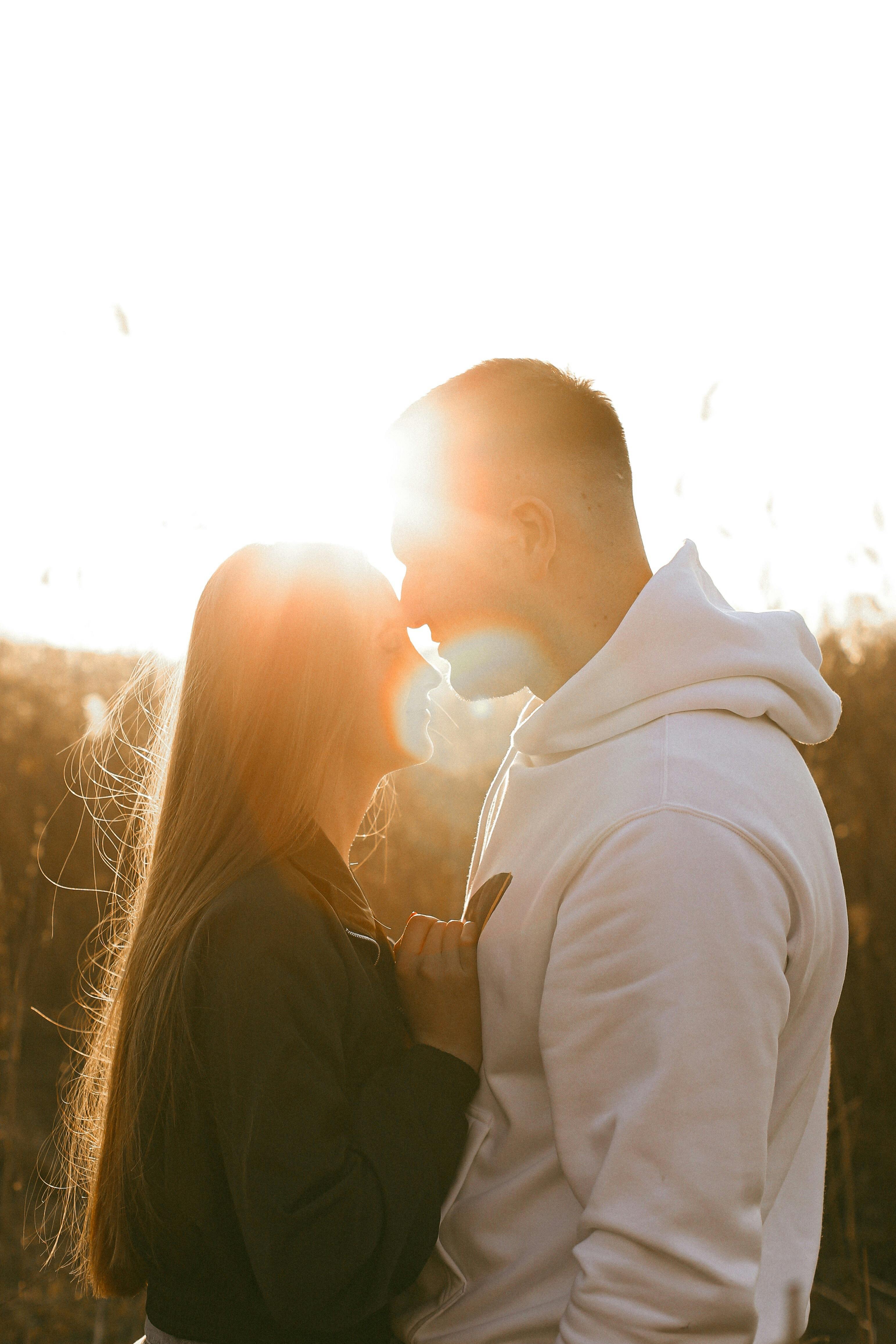 A couple shares an intimate moment, embracing in a sunny outdoor setting.