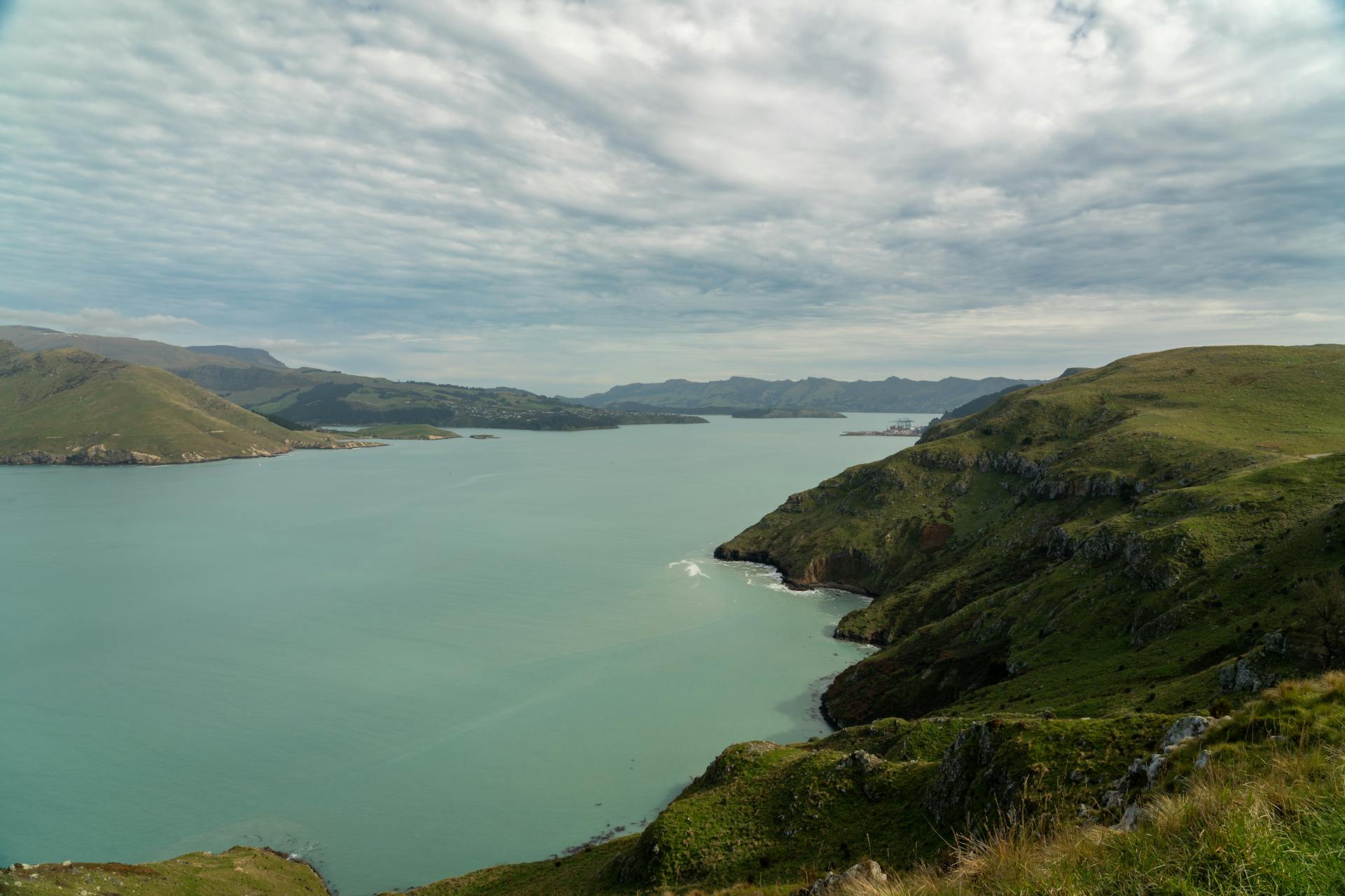 Scenic view of Lyttelton Harbour with rolling hills and cloudy sky in Canterbury, New Zealand.